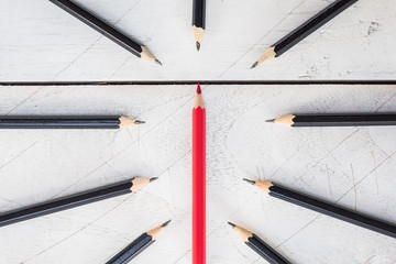 Red pencil standing out from crowd of plenty identical black fellows on white table. Leadership, business success concept