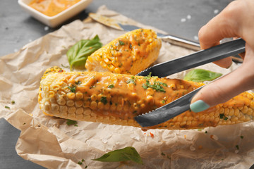 Female hand taking tasty grilled corncob from parchment by using tongs, close up view