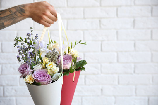 Male hand holding beautiful bouquets on blurred brick wall background