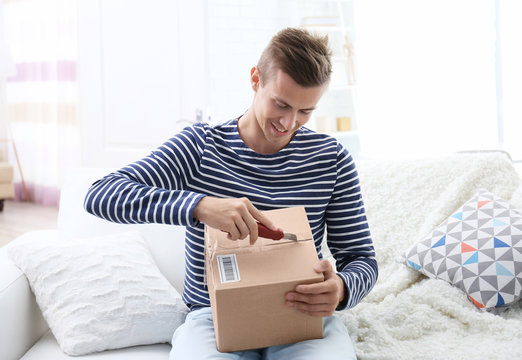 Young man sitting on sofa and unpacking received parcel