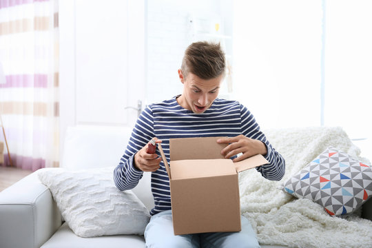 Young man sitting on sofa and unpacking received parcel