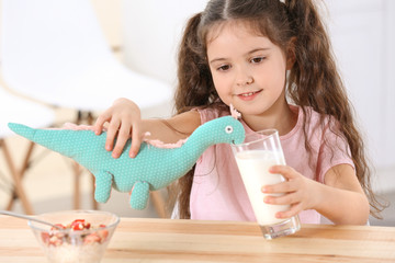 Cute little girl playing with toy dinosaur at kitchen table
