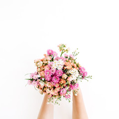 Girl's hands holding wildflowers bouquet on white background. Flat lay, top view