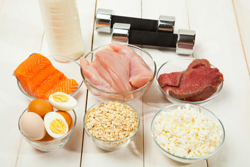 Protein diet, fish, cheese, eggs, meat, chicken and dumbbells on a white wooden background