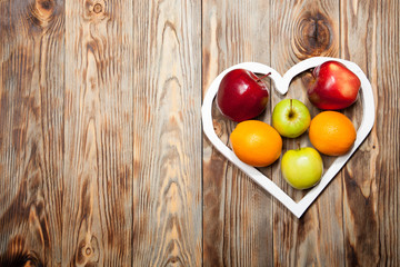 White heart, apples and oranges on the wooden background