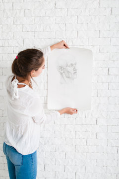 Woman looking at pencil portrait against wall. Artist evaluating her performance in workshop, new drawing style training. Art, study, creativity, criticism, craft concept