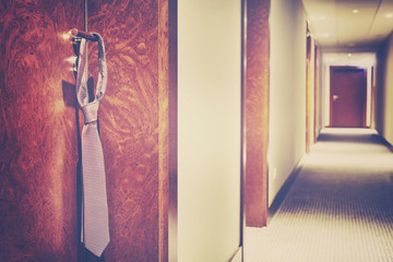 Vintage stylized tie hanging on a hotel closed door handle