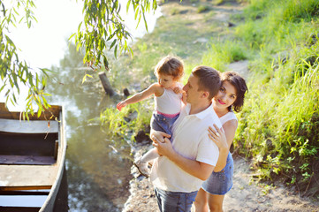Naklejka na ściany i meble Family portrait - mother, father and daughter on the river Bank near the boat.