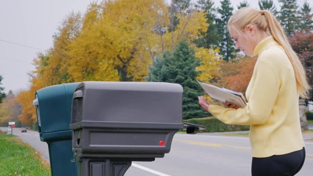 Yong caucasian woman takes the mail from the mailbox. Countryside in USA