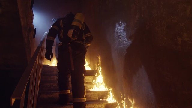 Two Strong Firefighters Going Up The Stairs in Burning Building. Stairs Burn With Open Flames. In Slow Motion.  Shot on RED EPIC (uhd).