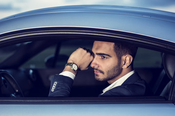 Portrait of young attractiave man in business suit sitting in his new stylish car outdoor in countryside