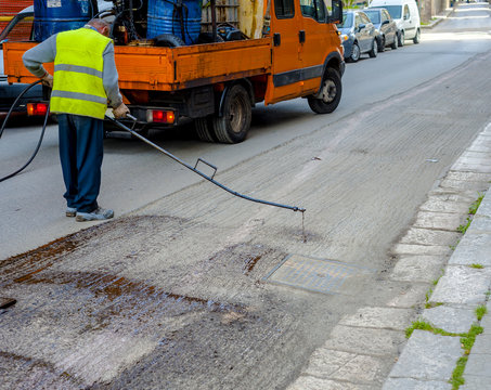 Road worker spraying bitumen emulsion with the hand spray lance before applying a new layer of asphalt