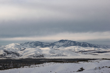Winter snow mountain valley with rocky hills under cloudy gloom sky. Altai Mountains, Siberia, Russia