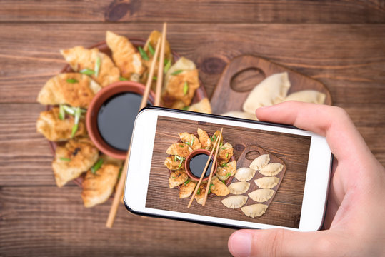 Hands taking photo homemade сhicken potstickers with soy sauce with smartphone.