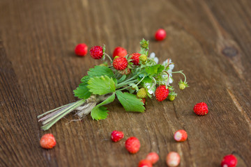 Fototapeta na wymiar Bush of wild strawberry with berries and flowers on wooden background