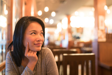 Tanned Asian girl thinking and looking upward to copy space, wondering menu to order for dinner,...