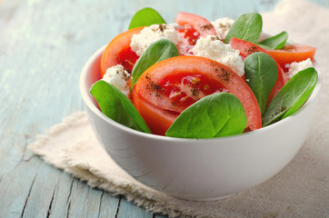 Tomato salad with spinach, cottage cheese, olive oil and pepper on blue wooden background