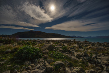 The rocky shore of Lake Tekapo under the moon light with Southern Alps in the background