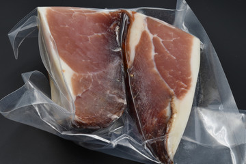 A big piece of Italian speck in a vacuum packing. Black background.