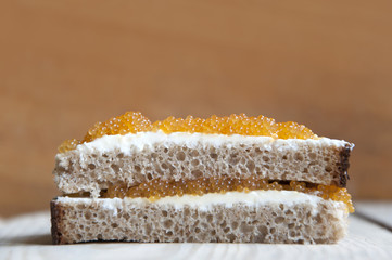 Multilayer sandwich of bread, cream cheese and pike caviar close-up on light wood surface. Side view, empty place.