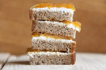 Multilayer sandwich of bread, cream cheese and pike caviar close-up on light wood surface. Side...