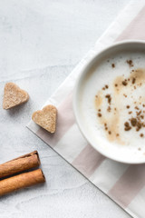 Cup of cappuccino with brown sugar and a cinnamon sticks on concrete background. Top view. Vertical photo