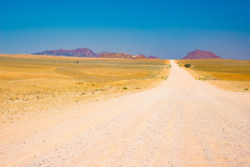 Fototapeta na wymiar Gravel 4x4 road crossing the colorful desert at Twyfelfontein, in the majestic Damaraland Brandberg, scenic travel destination in Namibia, Africa.