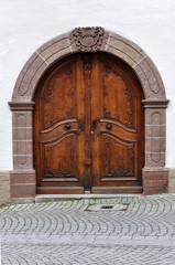 Arched wooden door of an old stone building with decorative carved elements. Waiblingen, Baden-Wurttemberg, Germany.