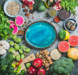 Fototapeta na wymiar Clean eating concept over grey background with bright blue plate in center, top view, copy space. Vegetables, fruit, seeds, cereals, beans, spices, superfoods, herbs for vegan, gluten free diet