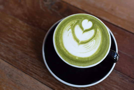 matcha green tea latte with heart shape latte art in black cup on wooden table