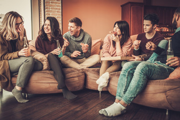 Group of multi ethnic young friends eating pizza in home interior