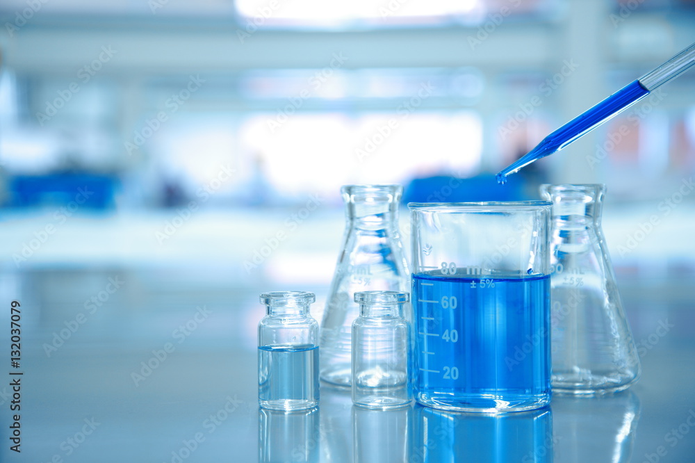 Wall mural blue drop into glass beaker with flask and science laboratory