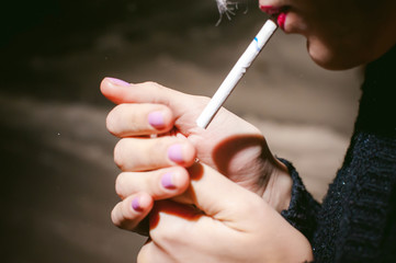 Portrait of a girl with a cigarette. young beautiful girl hipster with dyed hair smoking a cigarette in the street under the snow. her hands lights a lighter, lighting a cigarette tobacco
