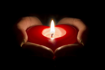 woman's hands holding a heart shaped candle in the dark