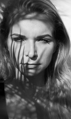 Fototapeta premium Black and white portrait photo of pretty blonde woman with palm tree leaves pattern shadow on her face and body