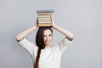 Girl with a stack of books showing tongue. Joking during study