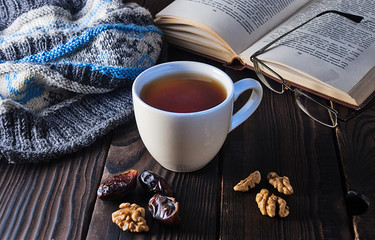 Cup of tea, book and knit cap on wooden table