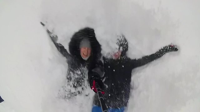The guy and girl falls in the snowdrift. Selfie with monopod