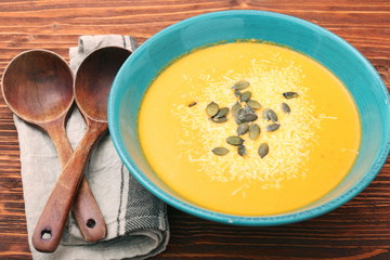 Pumpkin and carrot soup with cream and parsley on dark wooden ba