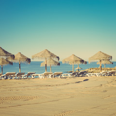 Holiday and vocation image with sandy beach, parasol and chairs on outdoors background