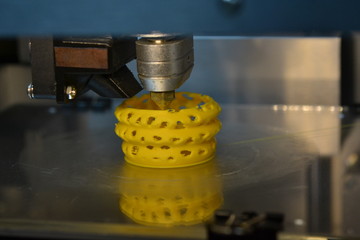 3D printer prints yellow form figure close. Automatic three dimensional 3d printer performs plastic...