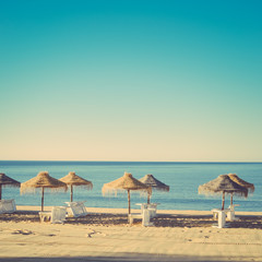 Holiday and vocation image with sandy beach, parasol and chairs on outdoors background