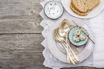 Culinary background. Serving for dinner with quail eggs, dishes silverware, fresh bread on a vintage tablecloth handmade. Top view