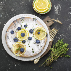 Comfort food. Homemade flavored sponge cake with blueberries and slices of lemon on a marble background. Top
