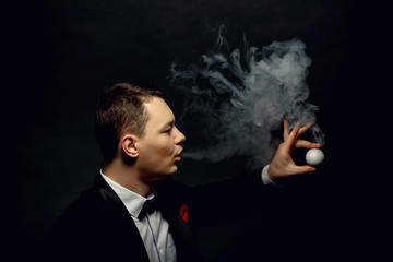 Illusionist man makes smoke his hand on a dark background.
