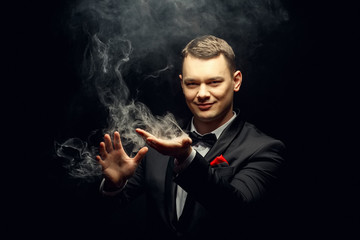 Illusionist man makes smoke his hand on a dark background.