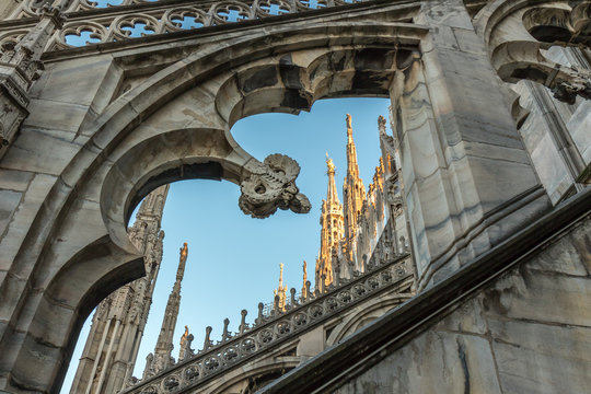 Details of marble spiers and statues of Milan Cathedral, Italy, at sunset.