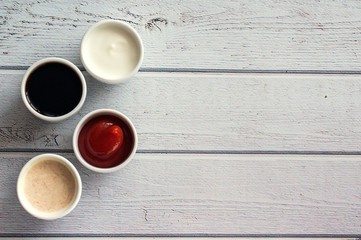 Fototapeta na wymiar Sauces ketchup, mustard, mayonnaise, sour cream, soy sauce in clay bowls on wooden white background