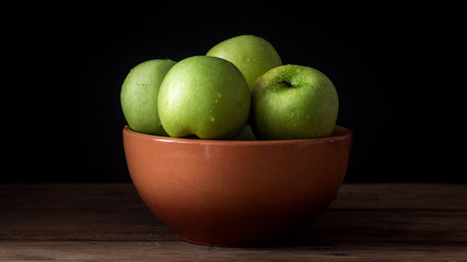 fresh green apple with droplets of water in bowl against black background