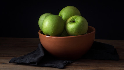 fresh green apple with droplets of water in bowl against black background